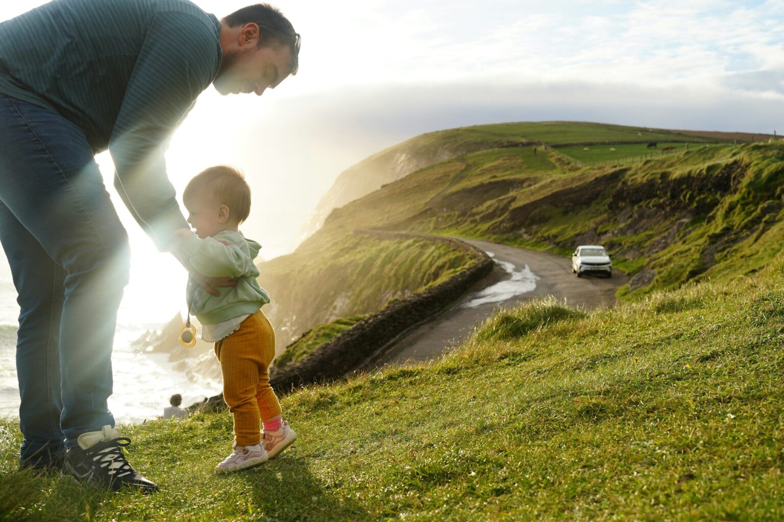 Father helps his child walk near a scenic cliff.
